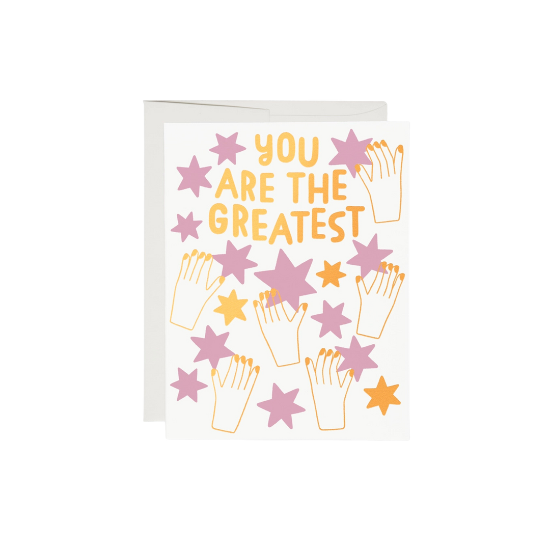 This 5.5"x4.25" card has a stars and says you are the greatest. gold illustration of hands holding pink and gold stars. 100lb heavyweight card stock, foil-stamped offset printing, and a design illustrated by Anke Weckmann. Additionally, this card is blank inside and printed in the USA on recycled paper.
