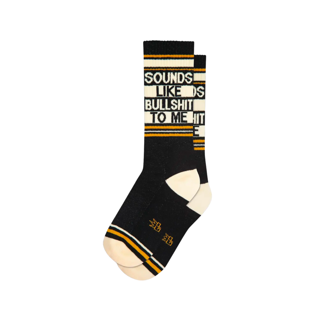 Black socks with yellow and white stripes and text "Sounds Like Bullshit To Me". Recently, have you felt continually lied to? Sounds Like Bullshit To Me socks know how that feels. With their comfortable nylon/cotton/spandex blend fabric and unisex, one size fits most design, you'll be sure to be comfy while you're being lied to. Manufactured in the USA.