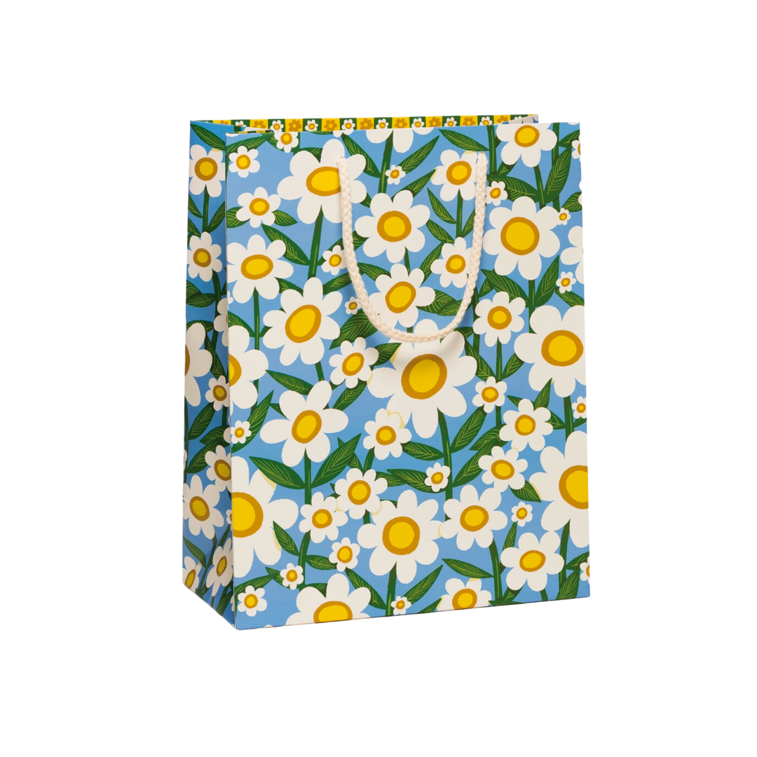White flowers with green stems on blue background white rope handle. 10 x 5 x 12.75 in. Made with premium, heavyweight coated paper and equipped with a sturdy cotton rope handle, this gift bag features an illustration by artist Krista Perry.