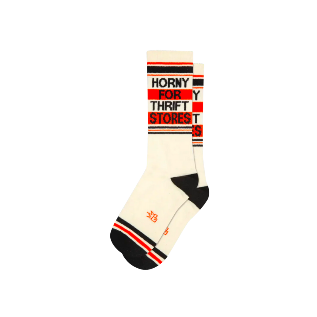 White socks with black and orange stripes and text "Horny For Thrift Stores". Seek out the vintage finds of your dreams with this statement piece. Crafted from a blend of cotton, nylon, and spandex, these unisex socks are designed to fit most and are proudly made in the USA. Slide them on and get ready to hunt for some hidden gems!